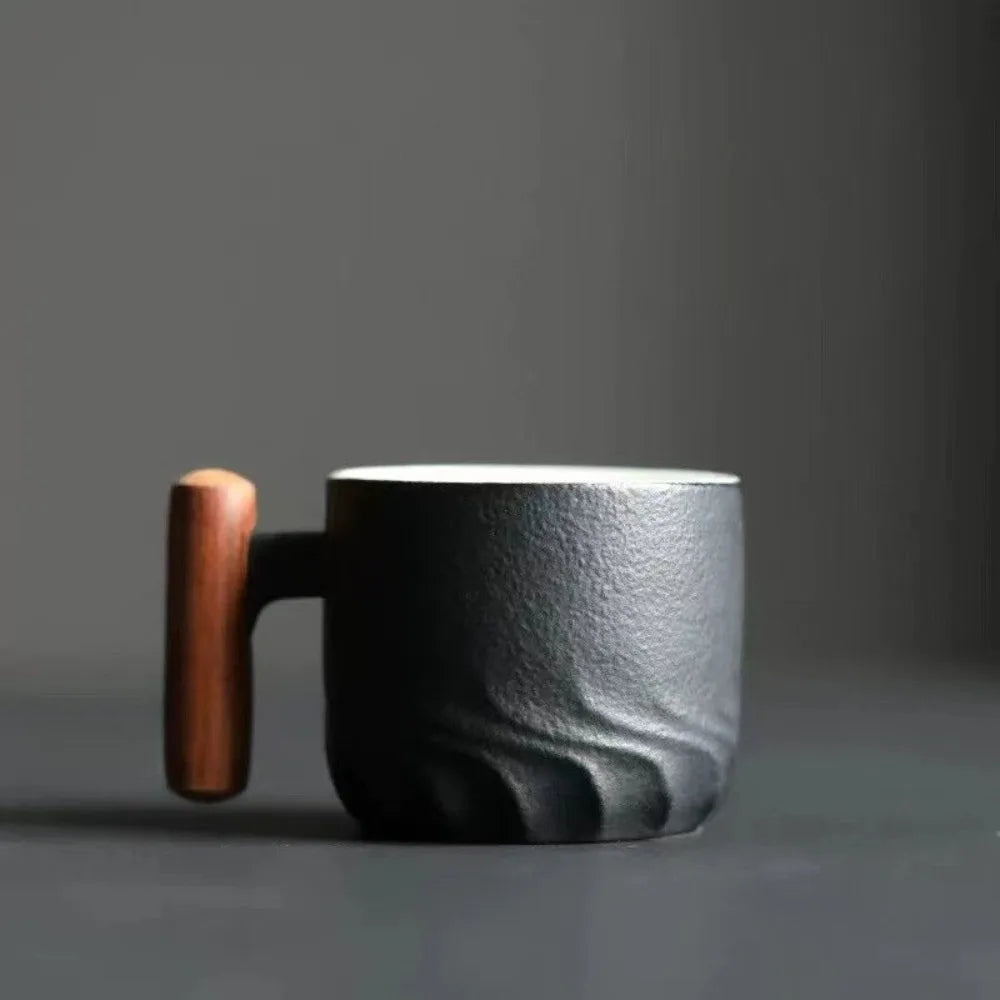 Handmade ceramic coffee cup with a textured black surface and a wooden handle for a unique touch