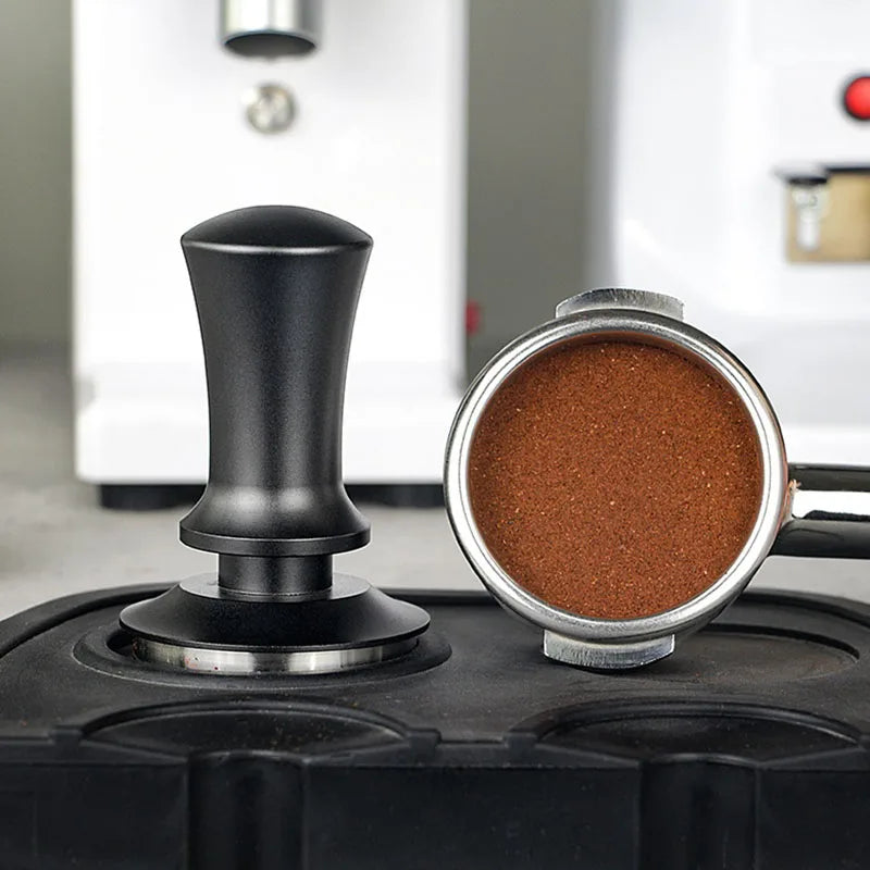stainless steel espresso tamper 51mm 53mm 58mm placed next to a coffee portafilter with ground coffee