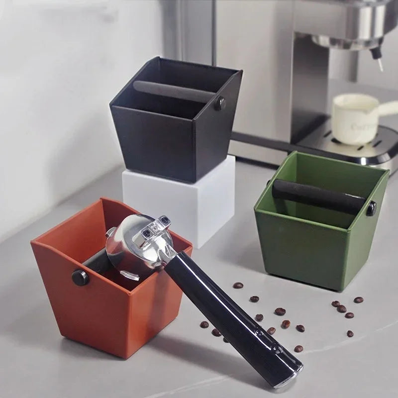 Set of four anti slip coffee knock boxes in black, white, green, and orange with coffee beans scattered nearby